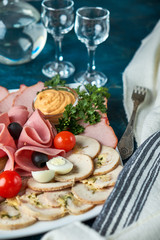 Cold smoked meat plate with prosciutto, salami, bacon, pork chops, cheese and olives on gray stone background.