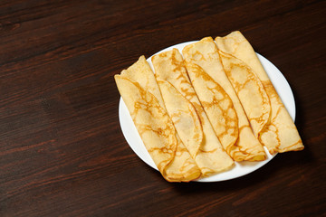 Crepe closeup, heap of thin pancakes on a dish, wood background