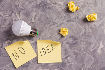 One modern new plastic led electric bulb and two yellow curved paper stickers with inscription no idea near three crumpled paper balls on old worn gray concrete floor. Business concept