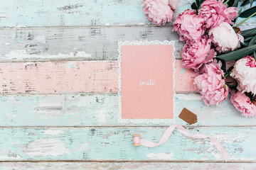 pink peony flowers with greeting card on wooden background. Minimal flat lay composition with copy space. © victoria
