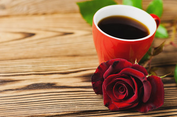Full cup of black coffee near one red rose on green sprig on old wooden table with copy space. Saint Valentine's Day concept