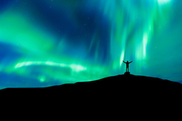 Aurora borealis with silhouette standing man on the mountain.Freedom traveller journey concept