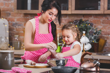 Young beautiful mother and her little daughter cooking together at the kitchen