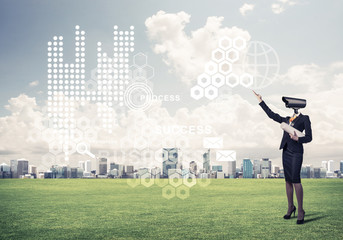 Camera headed woman standing on green grass against modern citys