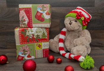 Teddybär mit Weihnachtsmütze sitzt zwischen Geschenken und Weihnachtsbaumkugeln