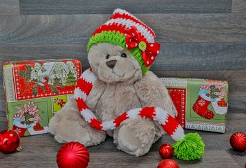 Teddybär mit Weihnachtsmütze sitzt zwischen Geschenken und Weihnachtsbaumkugeln