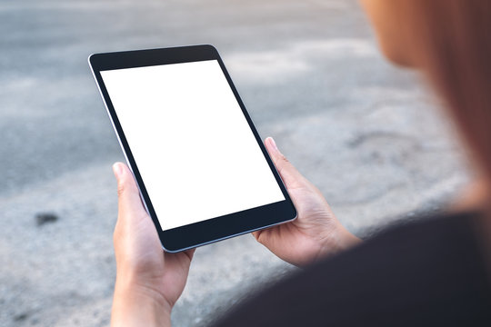 Mockup image of a woman holding and looking at black tablet pc with blank white screen with street background