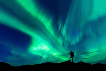 Obraz na płótnie Canvas Aurora borealis with silhouette standing photographer on the mountain.Freedom traveller journey concept