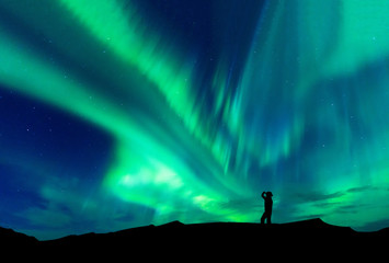 Naklejka na ściany i meble Aurora borealis with silhouette standing man on the mountain.Freedom traveller journey concept