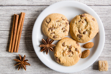 Tasty cookies with chocolate crumbles, anise stars spices, brown sugar and cinnamon rolls on wooden background, top view. Winter Christmas mood.