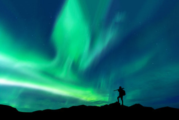 Obraz na płótnie Canvas Aurora borealis with silhouette standing photographer on the mountain.Freedom traveller journey concept