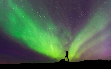 Obraz na płótnie Canvas Aurora borealis with silhouette standing man on the mountain.Freedom traveller journey concept