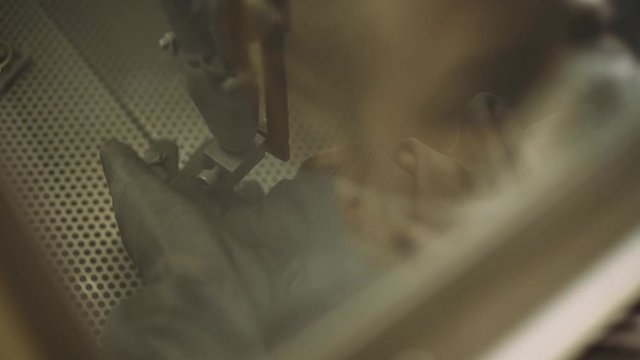 Production of watches, female worker controls the sandblasting machine, machining steel watch case, view through the glass.
