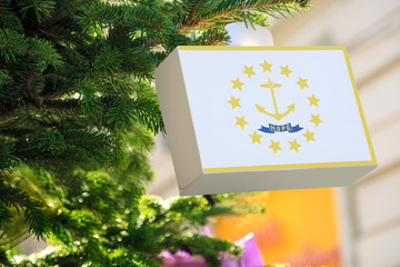 Rhode Island state flag printed on a Christmas gift box. Printed present box decorations on a Xmas tree branch on a street. Christmas shopping in United States, local market sale and deals concept.