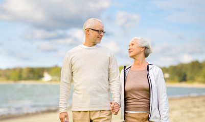 Naklejka premium old age, retirement and people concept - happy senior couple over beach background