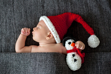 Little sleeping newborn baby boy, wearing Santa hat and holding toy