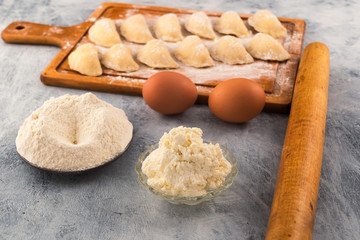 Ingredients for cooking dumplings with filling-flour and cottage cheese in plates, chicken eggs, rolling pin for rolling dough.