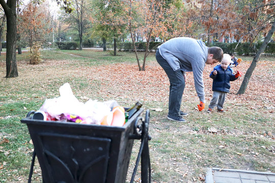 Father and little son scavenging in the park. Background - trash and litter bin. The concept of ecology and protecting the planet from debris