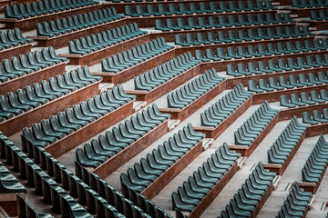 Free unclaimed seats in multiple rows. Sunset photo in empty public arena and concert amphitheatre. Red brick and white travertine structure, gray plastic chairs. 