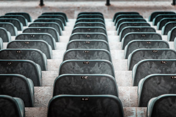 Fototapeta premium Free unclaimed seats in multiple rows. Sunset photo in empty public arena and concert amphitheatre. Red brick and white travertine structure, gray plastic chairs. 