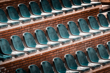 Free unclaimed seats in multiple rows. Sunset photo in empty public arena and concert amphitheatre. Red brick and white travertine structure, gray plastic chairs. 