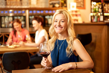 people, alcohol and lifestyle concept - happy woman drinking red wine at restaurant or bar