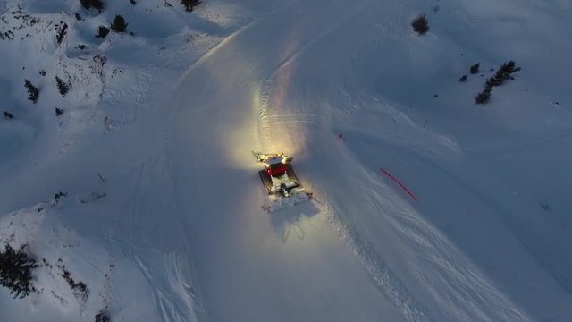 Aerial drone shot of a snow groomer in action. Low light end of the day. French Alps France.
