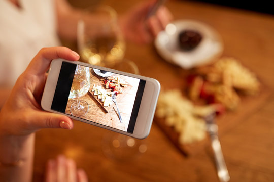 people, technology and lifestyle concept - hand picturing food by smartphone at wine bar