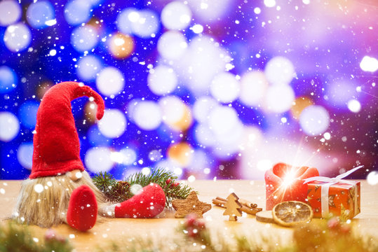 Christmas dwarf in falling snow with bokeh lights in background with ignited advent candle