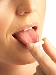 YOUNG WOMAN HOLDING WHITE PARACETAMOL TABLET ON TONGUE IN CLOSE UP