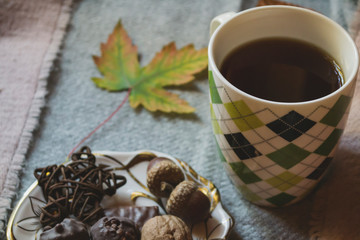Fototapeta na wymiar A cup of tea and sweet snacks with decoration by autumn leaves on the warm plaid. Seasonal still life.