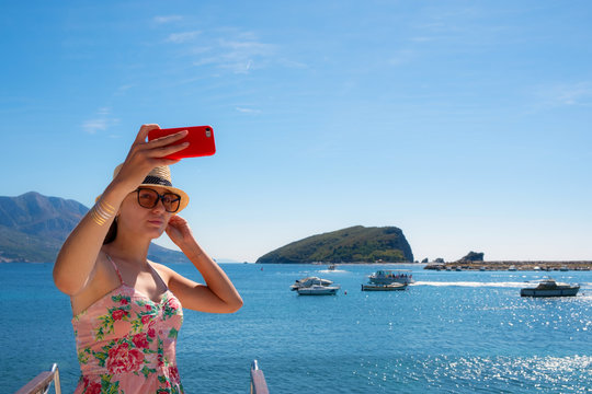 Young beautiful brunette girl in hat making selfie using phone while standing on the luxury yacht