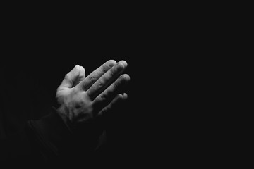 Hands of religious man praying on dark background, black and white effect