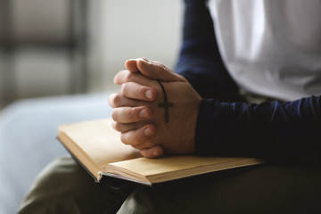 Religious young man with Bible praying at home, closeup