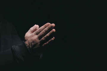 Hands of religious man praying on black background