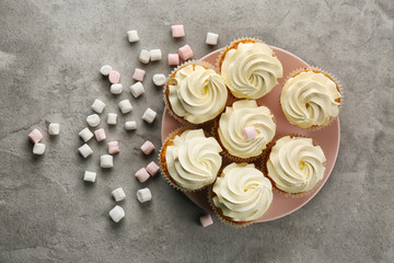 Plate with sweet cupcakes and marshmallows on grey table