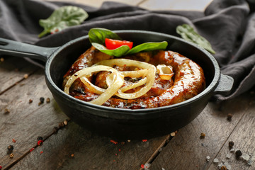 Frying pan with delicious roasted sausage and vegetables on wooden table