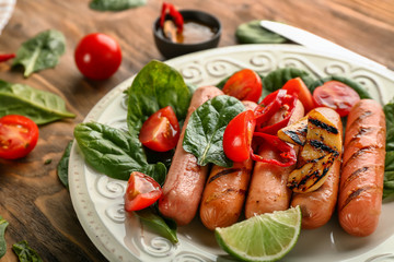Plate with delicious grilled sausages and vegetables on wooden table, closeup
