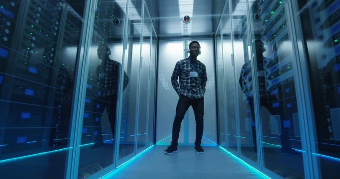 Young African American male IT specialist in headphones dancing in corridor of server room having fun