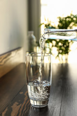 Pouring of fresh water from bottle into glass on wooden table