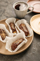 Plate with tasty eclairs and cup of coffee on grey table