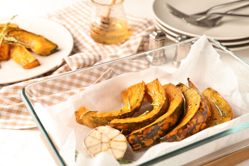 Glass dish with tasty baked pumpkin pieces on table