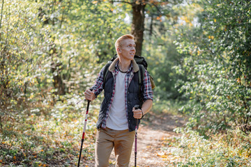 Young man enjoying hiking alone with nordic walking sticks in the forest