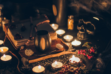 A ritual halloween witchcraft scene with candles, herbs, spider web, vintage bottles on the rustic background with a scary skull face and antique book