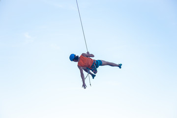 View of man in hardhat hanging on rope while doing rappel and showing pirouettes flying in air 