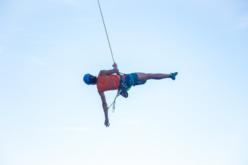 View of man in hardhat hanging on rope while doing rappel and showing pirouettes flying in air  © pablobenii