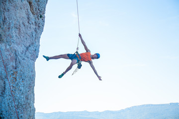 View of man in hardhat hanging on rope while doing rappel and showing pirouettes flying in air  © pablobenii