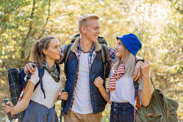 Group of happy best friends enjoying hiking together with huge backpacks and nordic sticks