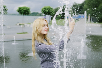 Obraz premium Portrait of beautiful student teenager girl holding up a smartphone taking selfies photos, networking using technology, outdoors park. Adolescent with books near water fountain, lifestyle exterior.
