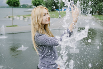 Portrait of beautiful student teenager girl holding up a smartphone taking selfies photos, networking using technology, outdoors park. Adolescent with books near water fountain, lifestyle exterior.